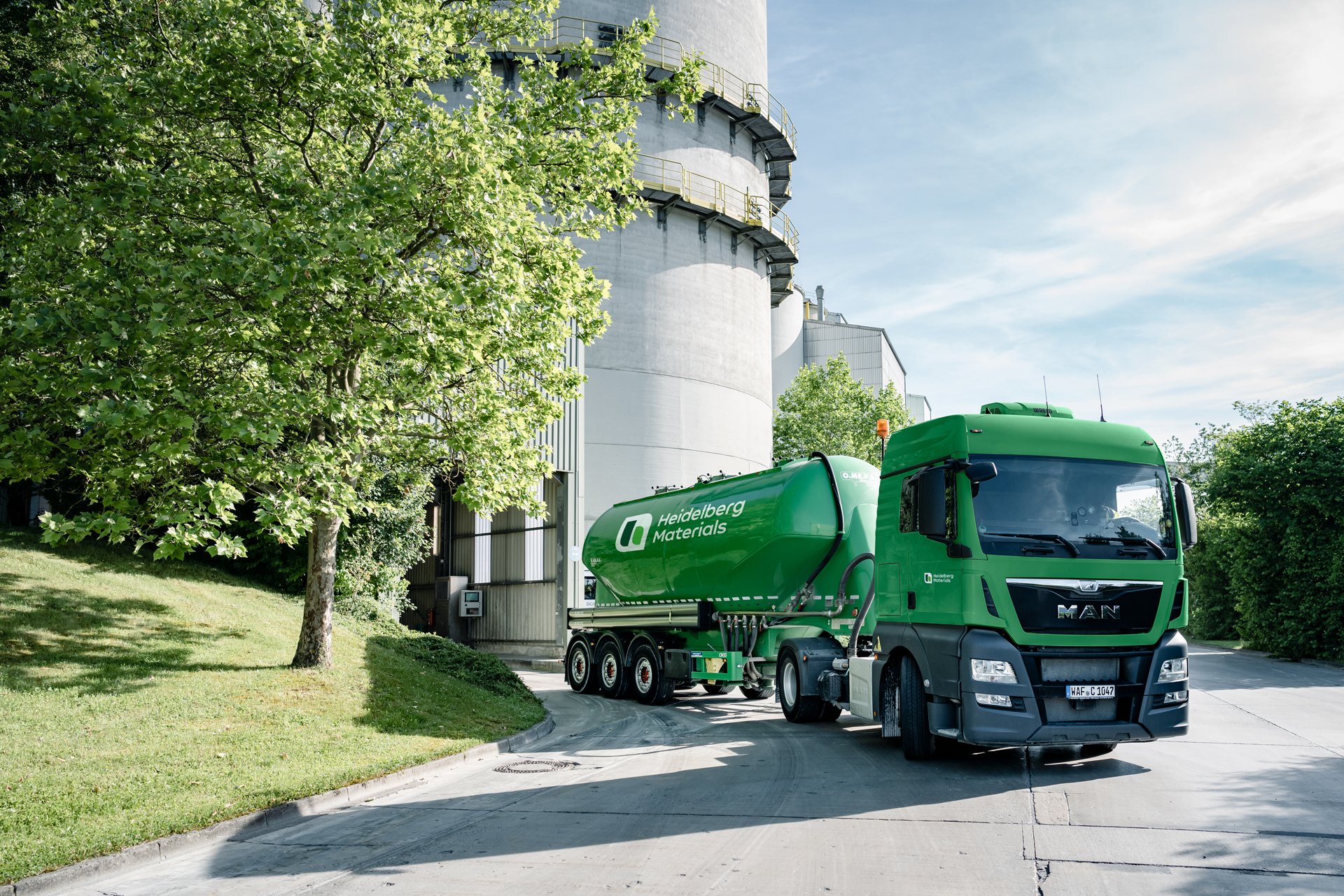 Grünes Silo-Fahrzeug vor einem Zementwerk